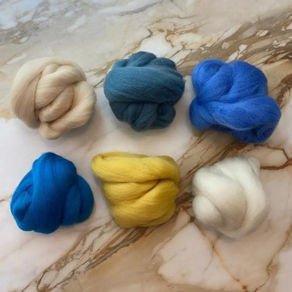 Six skeins of wool top spinning wool in blues, greens, golden yellow, white, and tan on marble