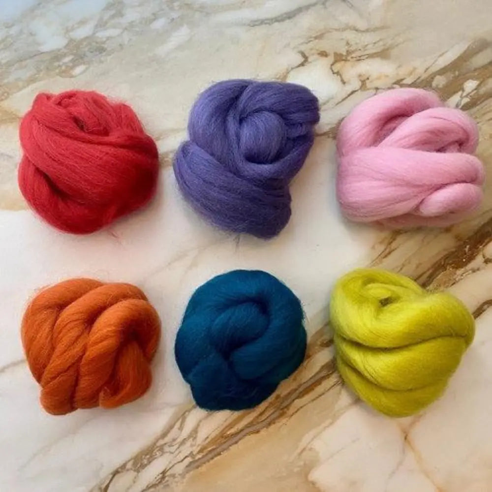 Six skeins of wool comb top in red, purple, pink, orange, blue, and yellow on marble background