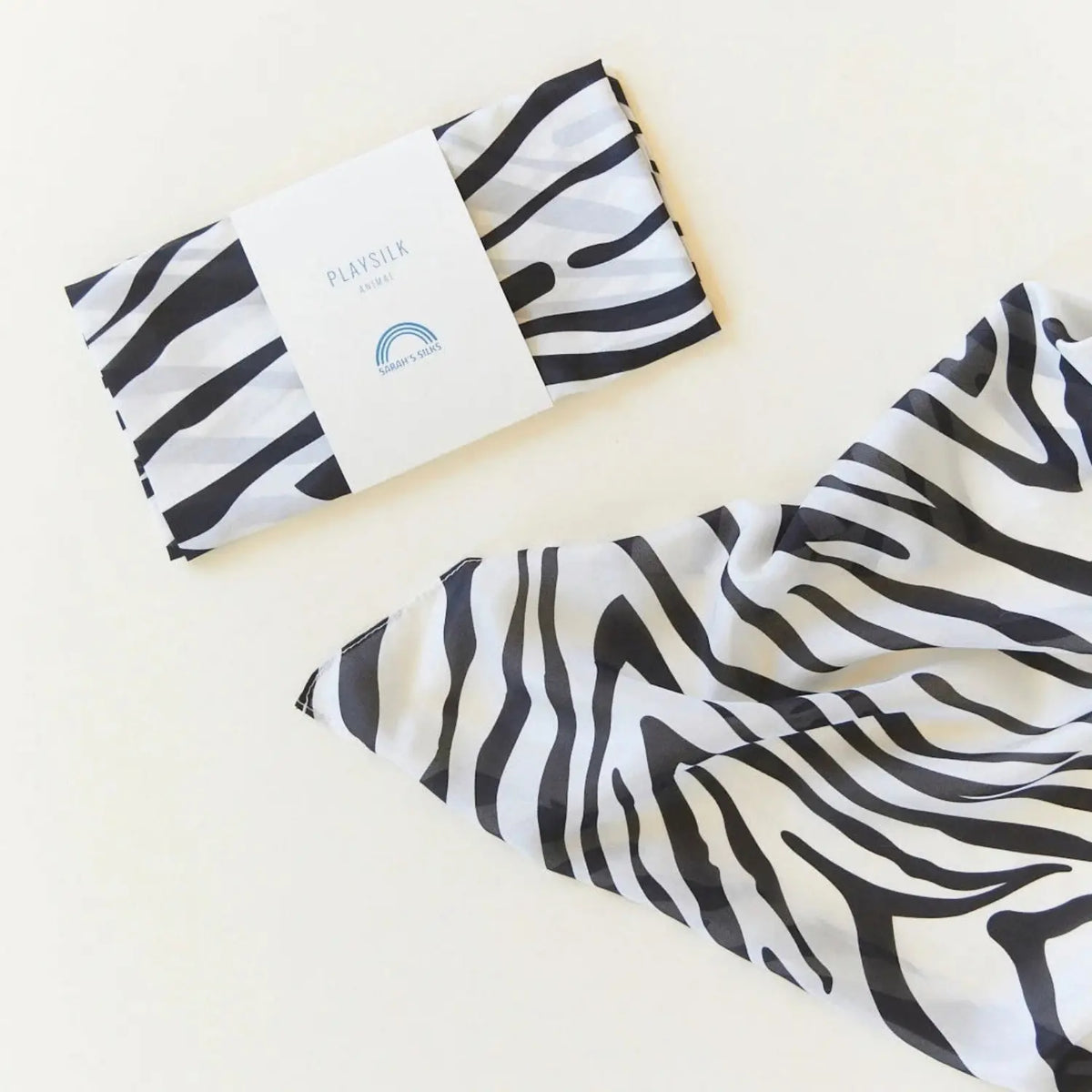 Sarah's Silks Zebra Playsilk in black and white animal print, folded with Playsilk packaging