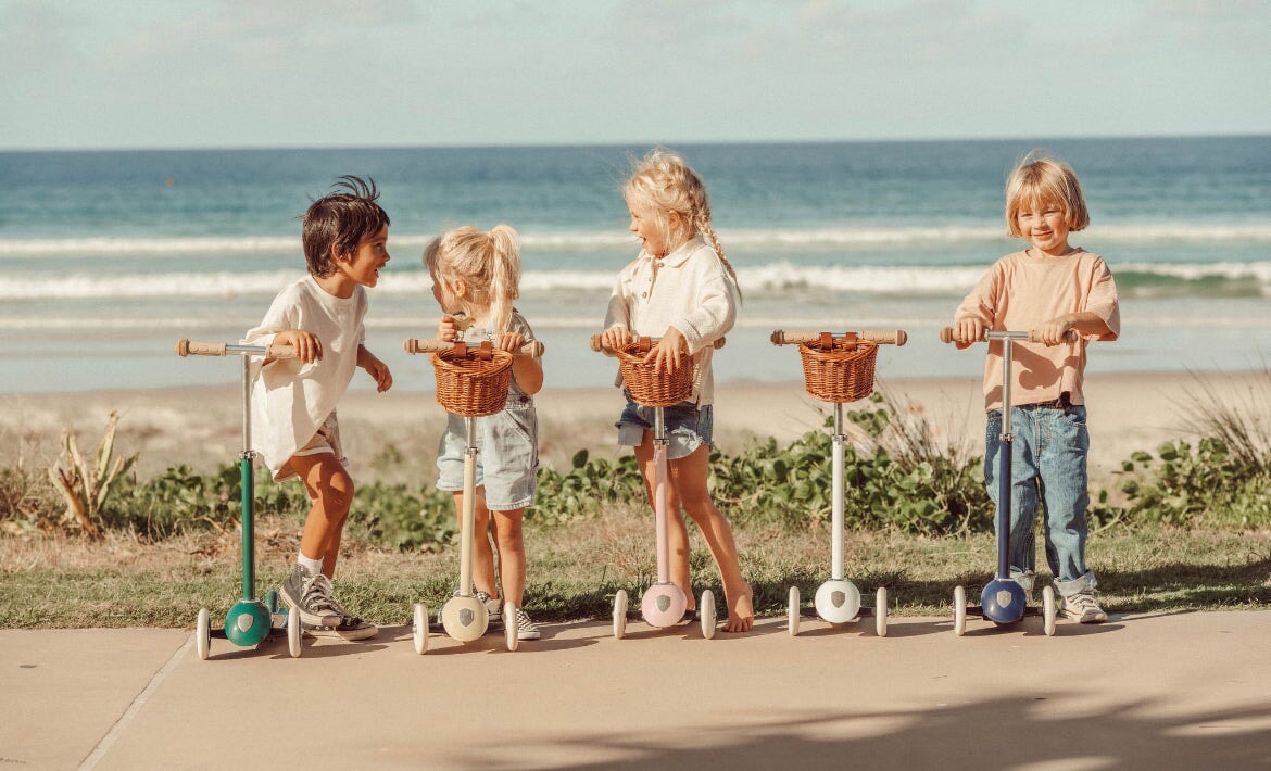 Banwood Three Wheel Scooter in four colors with kids with a beach background