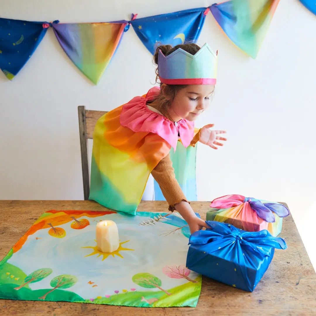 Child wearing a crown and cape with the Around the World Mini Playsilk with a candle in the middle