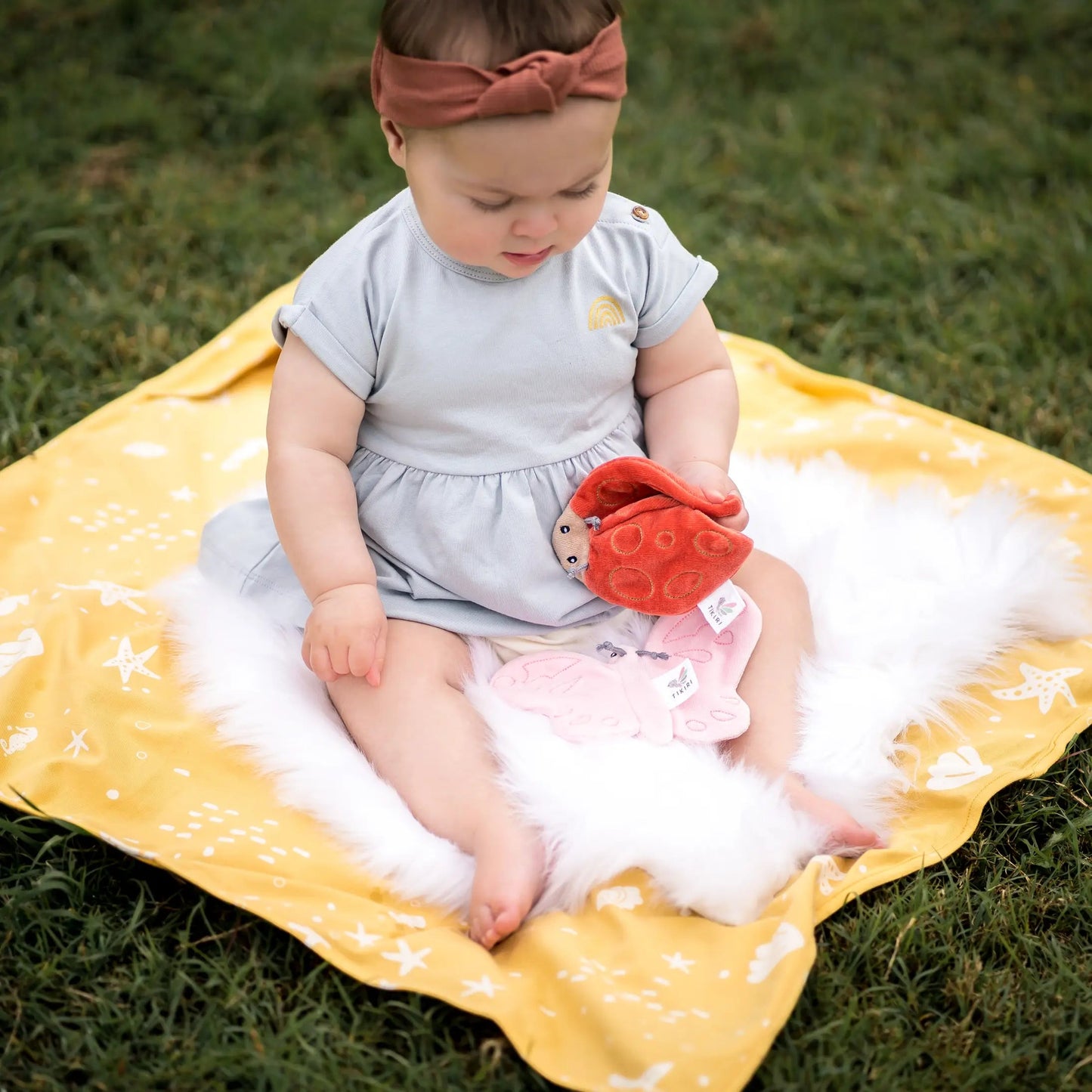 Tikiri Scrunchies - Baby on blanket in grass holding ladybug crinkle toy