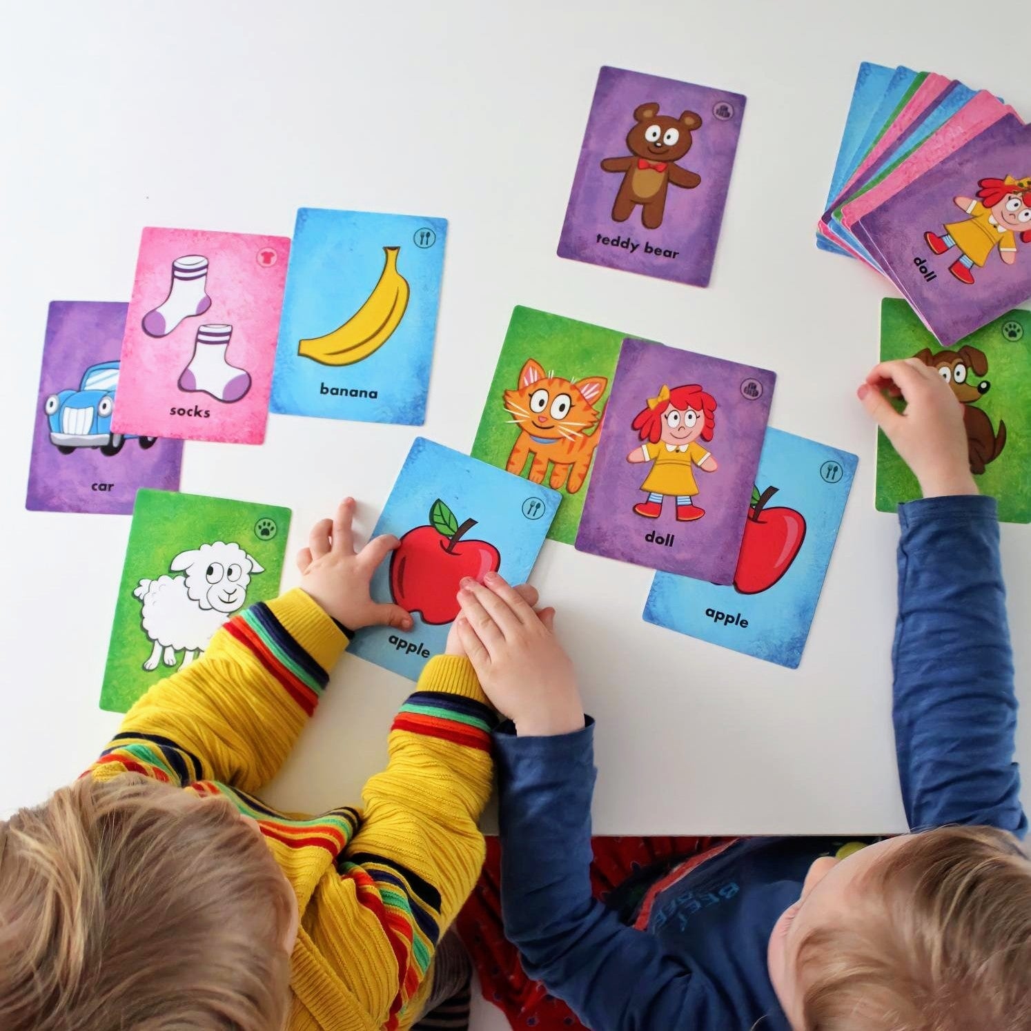 A Preschooler and Toddler playing Knock Knock card game on a white table
