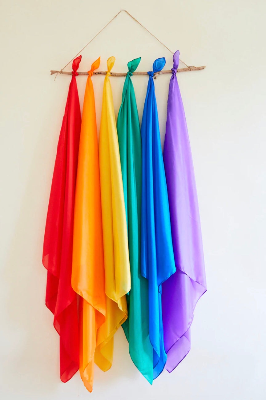 Playsilks in a rainbow of colors hanging from a wooden hanger