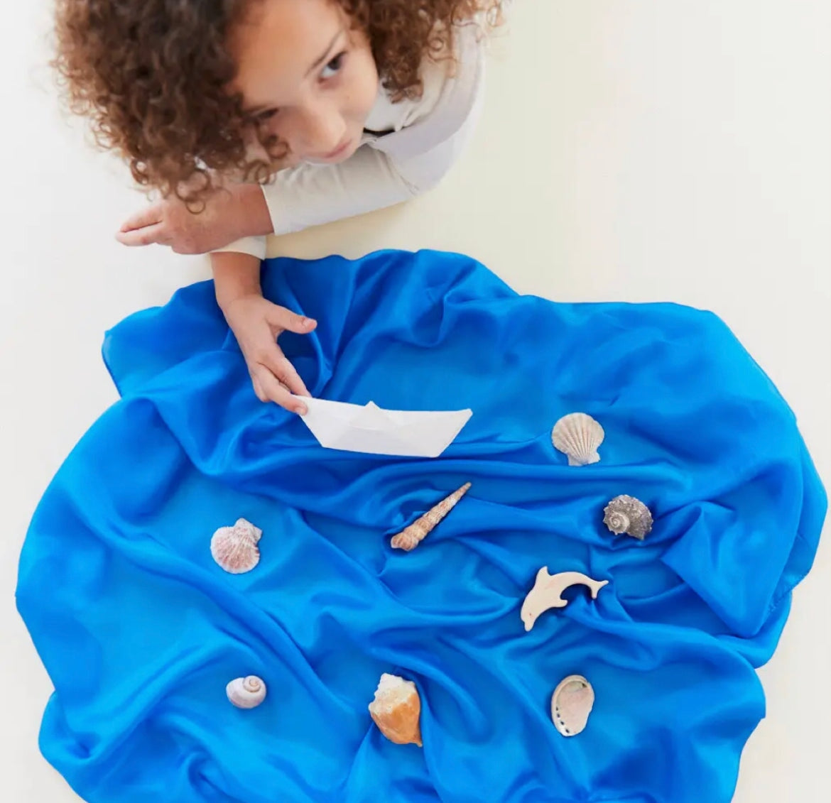 Playsilk in Royal Blue arranged as water with sea toys on top and a child playing