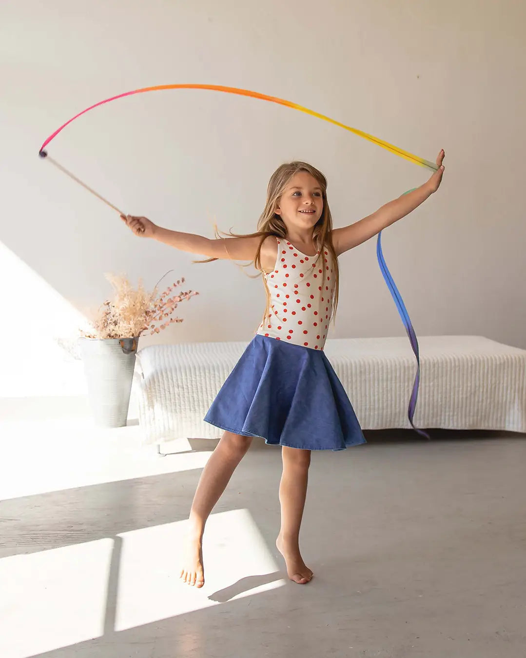Child waving a Sarah’s Silks Rainbow Streamer Wand indoors, creating a colorful arc through the air.