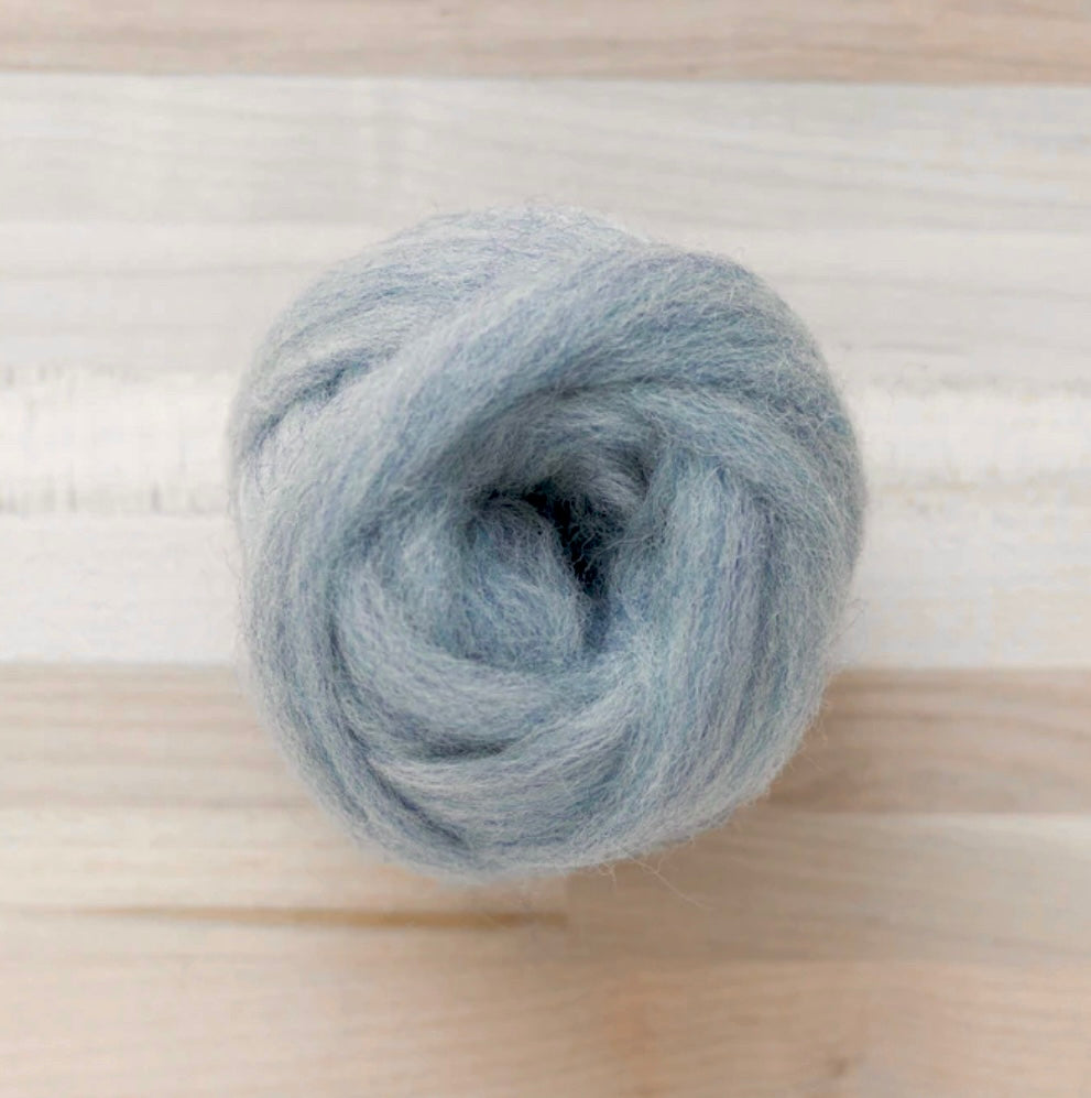 knot of wool roving in blue frost for needle felting on wooden background