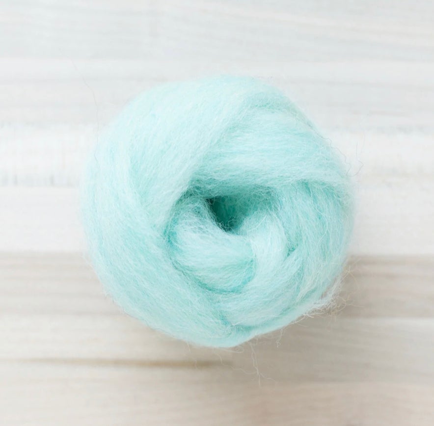 knot of spearmint green wool roving for needle felting on wooden background